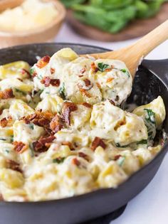 a skillet filled with pasta and spinach on top of a white tablecloth