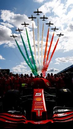 a red car with six jets flying in the sky above it and people watching from behind