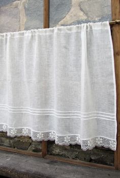 a white curtain hanging on the side of a window next to a stone wall with two pictures behind it