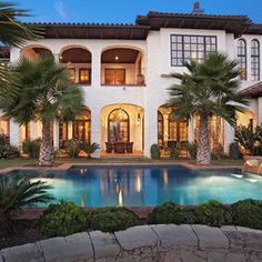 a large house with a pool in front of it and palm trees around the pool