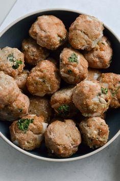 a bowl filled with meatballs covered in cheese and parsley on top of a table