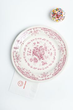 a pink and white plate with sprinkles on it next to a napkin