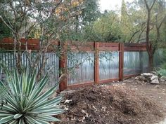 a fence that is next to a tree and some dirt in front of the fence