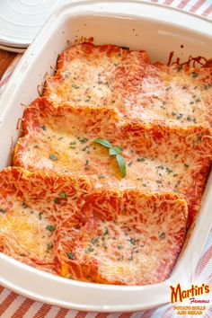 four slices of lasagna in a white casserole dish on a red and white tablecloth