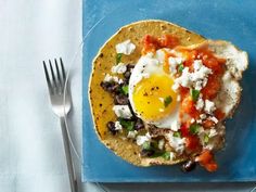 an egg is on top of a tortilla with tomatoes and black olives