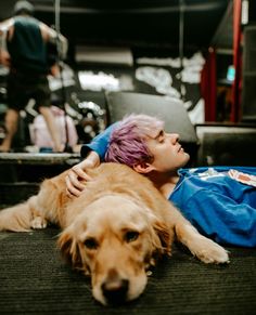 a person laying on the ground next to a dog with pink hair and blue shirt