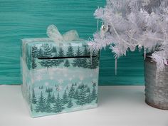 a present box sitting next to a christmas tree in front of a blue wall with snowflakes on it