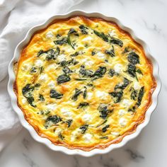 a quiche with spinach and cheese in a white dish on a marble surface