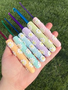 a hand is holding several colorful toothbrushes with daisies on them in the grass