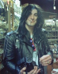 a man with long hair wearing a leather jacket and holding a camera in his hand