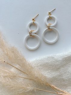 two white circular earrings sitting on top of a feather