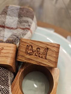 two wooden rings with initials on them sitting on a plate next to a plaid napkin