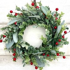 a green wreath with red berries and greenery hanging on a white wooden door frame