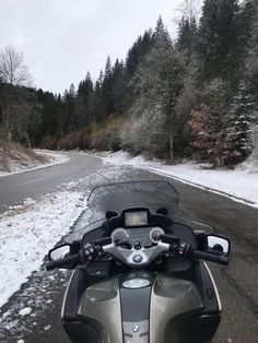 a motorcycle parked on the side of a road in front of snow covered ground and trees