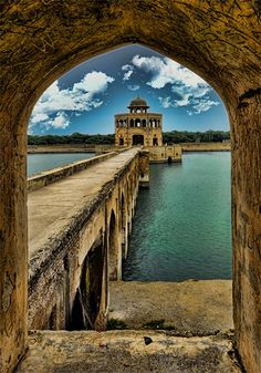 an arch in the side of a stone building with water below it and clouds above