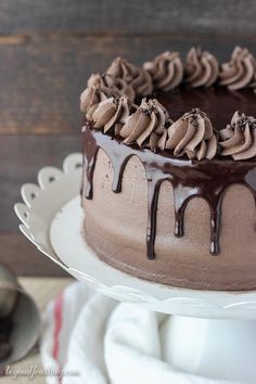 a chocolate cake sitting on top of a white platter next to a wooden table