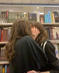 two people kissing each other in front of a book shelf with books on the shelves