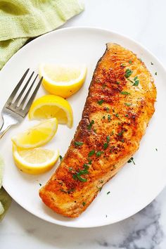 a piece of fish on a plate with lemons and a fork next to it