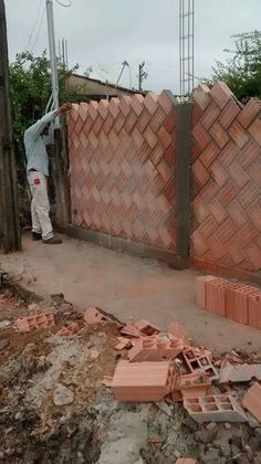 a man standing next to a pile of bricks on top of a dirt road near a fence