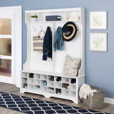 a white coat rack filled with coats and hats on top of a wooden floor next to a blue wall