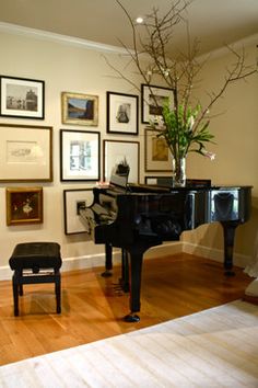 a black piano sitting in front of a wall with pictures on it and a vase filled with flowers