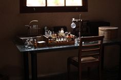 a table with bottles and beakers on it in front of a window, near a chair