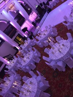 tables and chairs are set up for a formal function with purple lighting in the background