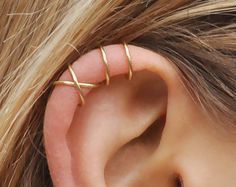 an ear piercing with three thin gold barbells on it's side, and the words handmade at amazon written below