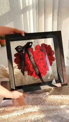 a person holding up a framed photo with red roses in the middle and black ribbon around it