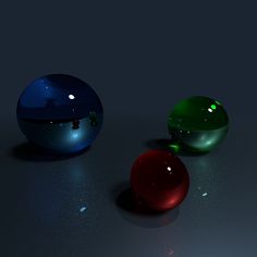 three different colored balls sitting on top of a black surface with light coming from them