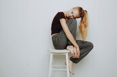 a young woman sitting on top of a white chair next to a wooden stool with her head down