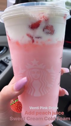 a woman holding up a pink drink with strawberries in it and ice cream on top