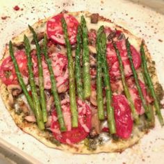 a pizza with asparagus, tomatoes and other toppings on top of it