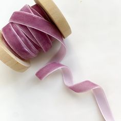 a spool of pink satin ribbon next to a spool of purple velvet tape