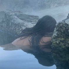 a woman is sitting in the water with her back turned to the camera and she has wet hair