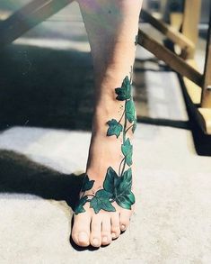 a woman's foot with green leaves on it and the bottom part of her leg