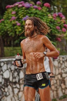 a man with long hair and no shirt on running in shorts while holding a water bottle