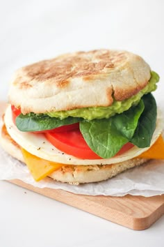 a sandwich with lettuce, tomato, and cheese on a wooden cutting board