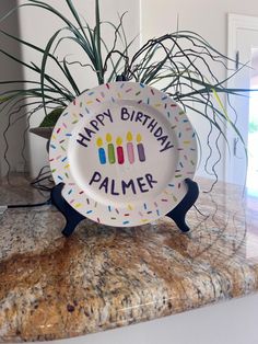 a happy birthday plate sitting on top of a counter next to a potted plant