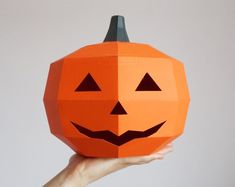 a hand holding an origami pumpkin with two faces on it's face