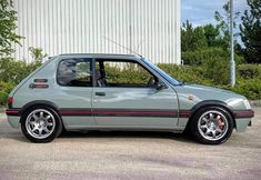 a grey car parked in front of a white building with red stripes on the rims