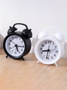 two black and white alarm clocks sitting on top of a wooden table next to each other