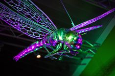 a green and purple light up insect hanging from the ceiling in front of a dark room