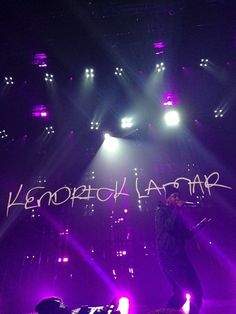 a man standing on top of a stage holding a microphone in his hand and writing on the wall behind him