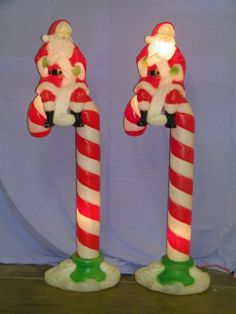 two lighted candy canes with santa clause on top and green base, both decorated in red and white stripes