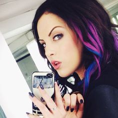 a woman with blue and purple hair is taking a selfie in her cell phone