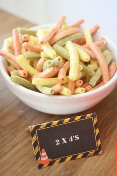 a bowl filled with pasta next to a small sign on a wooden table and an orange marker