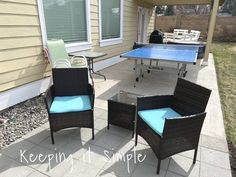 two wicker chairs and a ping pong table in front of a small house