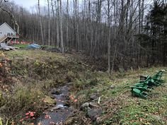 a house in the woods next to a small creek with green lawn chairs on it