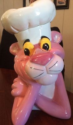 a pink and white cat figurine with a chef's hat on its head